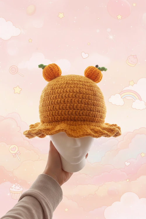 Yellow crochet hat with bear ears held by a hand against a soft, pastel background.